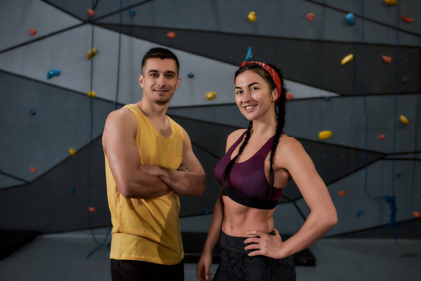 Elevate Your Mood. Active young man and woman in sportswear looking at camera, standing against climbing wall. Concept of sport life and rock climbing - Фото, зображення