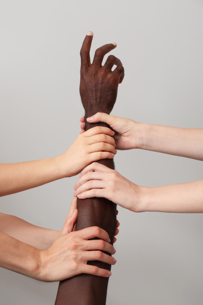 Białe kobiety trzymające za rękę Afroamerykanina na szarym tle. Koncepcja rasizmu - Zdjęcie, obraz