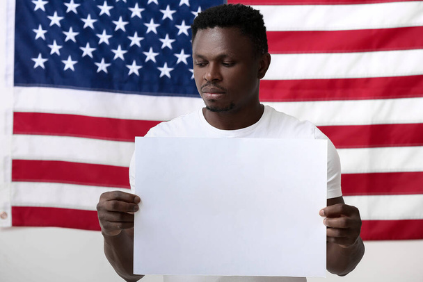悲しいアフリカ系アメリカ人の男性は、米国の国旗の近くにポスターを貼っています。人種差別をやめ - 写真・画像