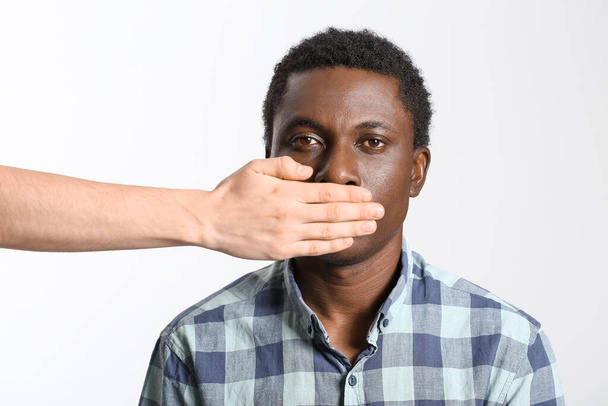 Persoon die de mond bedekt van een trieste Afro-Amerikaanse man op een lichte achtergrond. Stop racisme - Foto, afbeelding