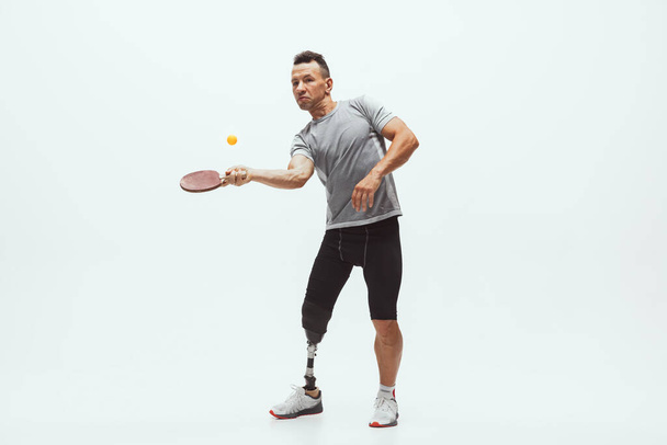 Athlete with disabilities or amputee isolated on white studio background. Professional male table tennis player with leg prosthesis training and practicing in studio. - Fotoğraf, Görsel