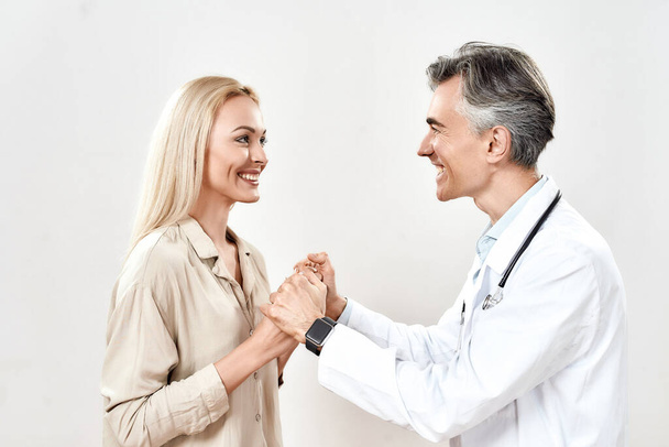 Medical care and support. Smiling mature male doctor in medical uniform holding hands of young happy female patient - Photo, Image