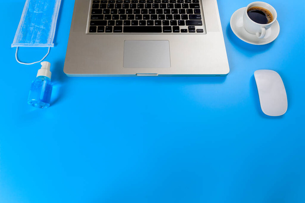 Arbeit von zu Hause aus. Laptop, schwarzer Kaffee. Maus, medizinische Gesichtsmaske, blaues Alkohol-Händedesinfektionsgel auf blauem Hintergrund mit Kopierraum. - Foto, Bild