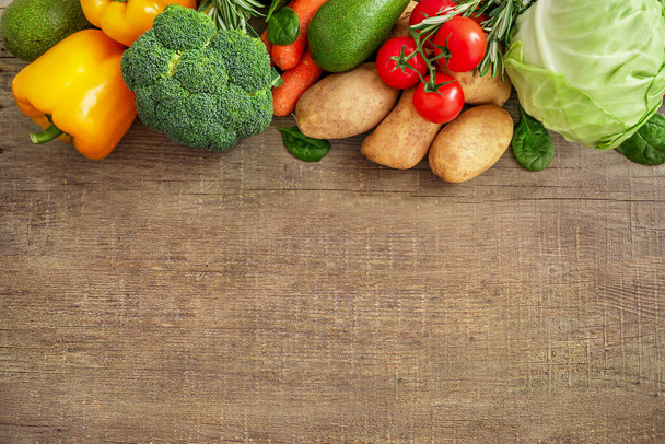 Асортимент сирих овочів на дерев'яному тлі: помідори, брокколі, капуста, авокадо, шпинат, жовтий перець, морква, картопля, розмарин. Вид зверху. Копіювати простір
. - Фото, зображення