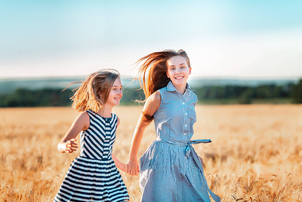 Happy teenage girls running down wheat field at the sunset - Foto, Imagen