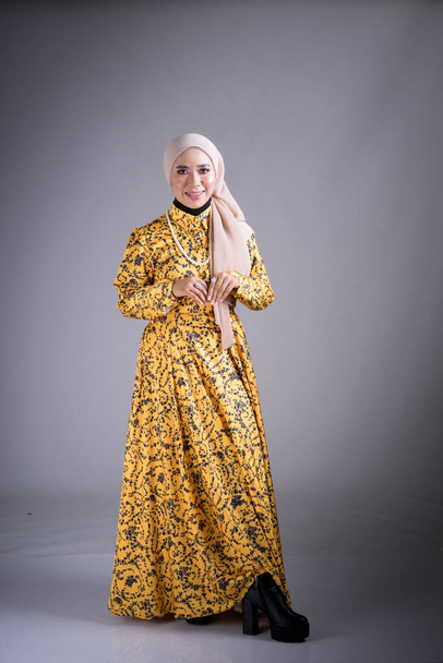 Full length portret van een mooi vrouwelijk model met traditionele jurk en hijab, een lifestyle kleding voor moslimvrouwen op grijze achtergrond. Idul Fitri en hijab modeconcept. - Foto, afbeelding