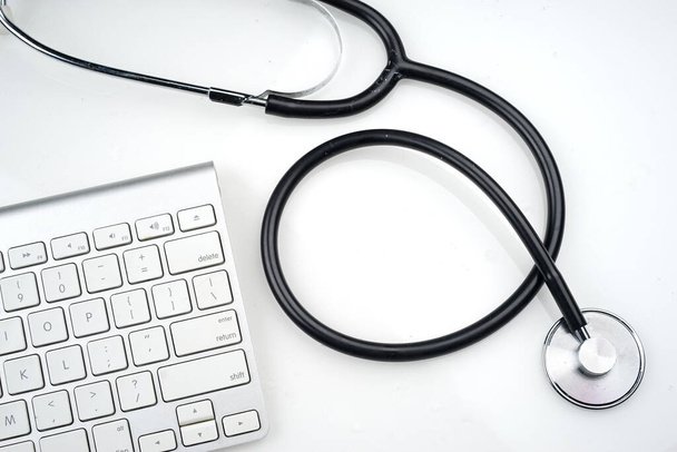Invoering van technologie in de gezondheidszorg. Stethoscoop en toetsenbord op witte achtergrond. Vlakke lay of bovenaanzicht. - Foto, afbeelding