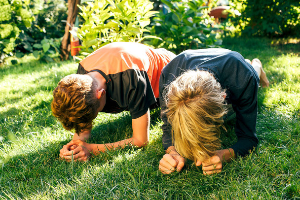 Dos chicos haciendo ejercicio de planchado sobre hierba en el jardín
 - Foto, imagen