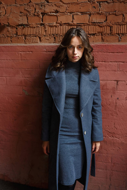 jeune fille réfléchie en manteau gris et pose col roulé devant le bâtiment rouge - Photo, image