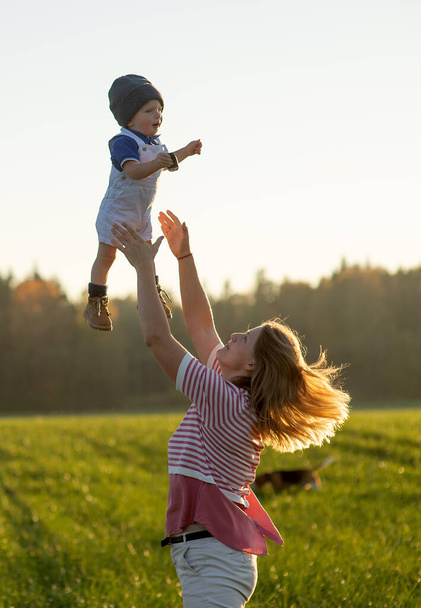 Happy harmonious family outdoors. Mother throws baby up, laughing and playing in the summer on the nature - Photo, image