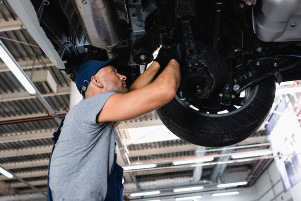 low angle view of technician in cap repairing car in service station  - Photo, Image