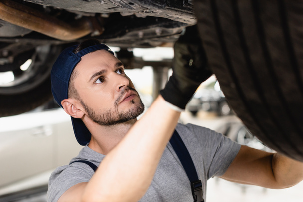 selective focus of mechanic in rubber glove and cap fixing car  - 写真・画像