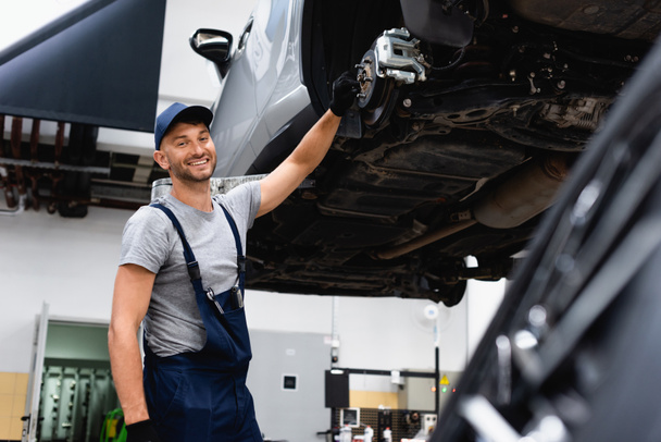 selective focus of happy mechanic in overalls standing near car  - Fotografie, Obrázek