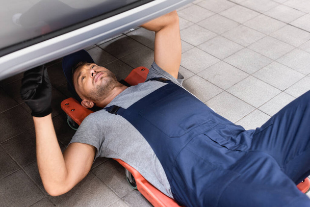 όμορφος μηχανικός ξαπλωμένος κάτω από το αυτοκίνητο στην υπηρεσία αυτοκινήτων  - Φωτογραφία, εικόνα