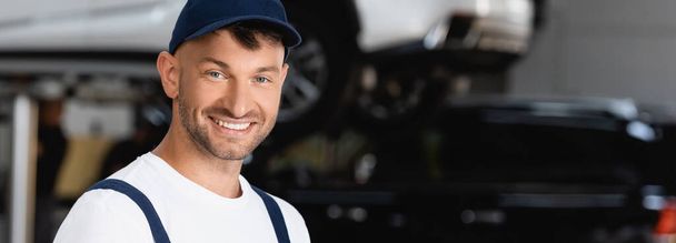 panoramic orientation of smiling mechanic in cap looking at camera - Photo, Image