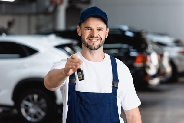 cheerful mechanic in uniform and cap holding car key  - Photo, Image