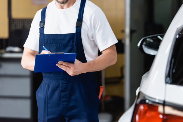 cropped view of mechanic in uniform holding clipboard near car - Photo, Image