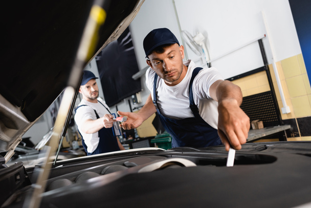 selective focus of mechanic in cap giving screwdriver to handsome coworker repairing car in workshop  - Фото, зображення
