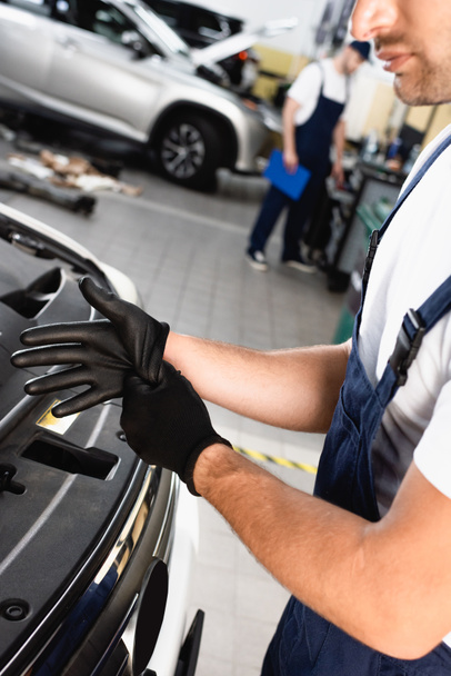 обрезанный вид механика в униформе в латексных перчатках возле автомобиля в мастерской  - Фото, изображение