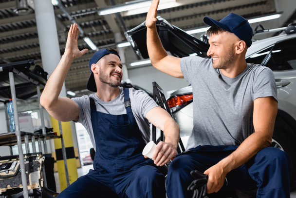 Glücklicher Automechaniker sitzt und gibt Kollegen an Tankstelle High Five - Foto, Bild