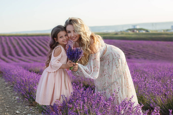pretty mother with daughter playing in lavender field. woman with child girl in sunset light gathering lavender flowers - Photo, Image