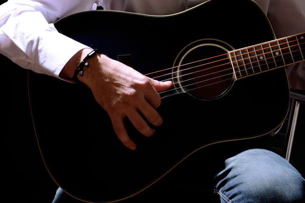 Young musician playing acoustic guitar, close up, on dark background - Foto, afbeelding
