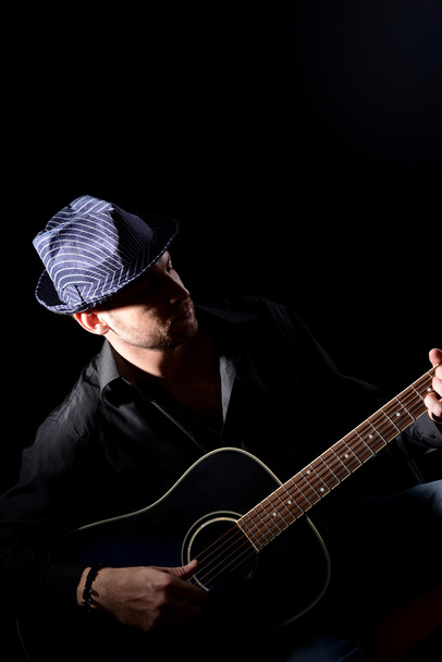 Young musician playing acoustic guitar and singing, on dark background - Photo, Image