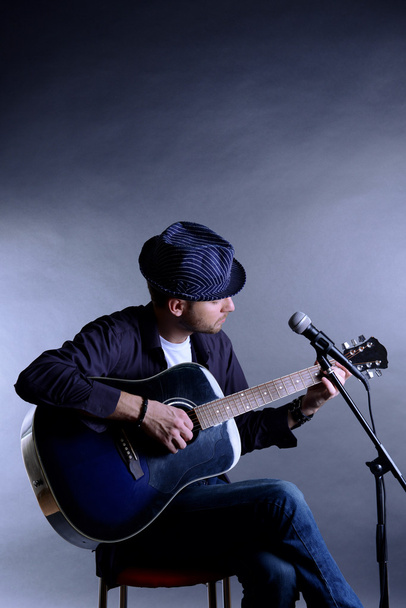 Young musician playing acoustic guitar and singing, on gray background - Foto, imagen