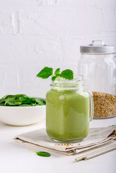 Vihreä smoothie juoda lasipurkissa valkoinen. Sekoitettu cocktail pinaatin ja vihreän tattarin kanssa. Terveellinen vegaaninen ruoka. - Valokuva, kuva