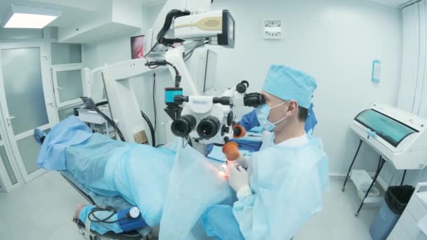 Cirujano mirando al microscopio en el ojo de la paciente femenina en el quirófano. Médico que usa microscopio durante el proceso de cirugía ocular, tratamiento de cataratas y corrección de dioptrías. - Metraje, vídeo