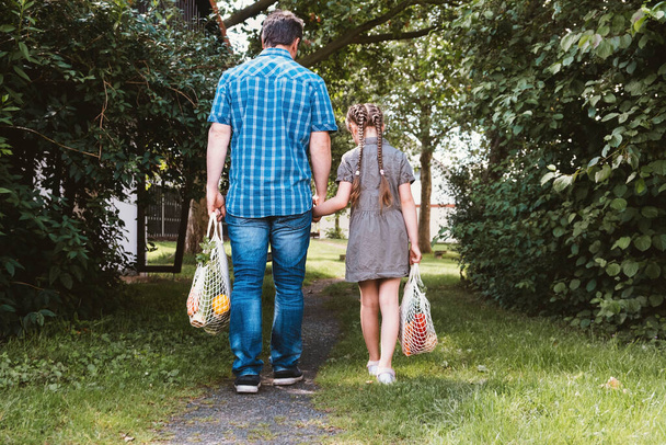 Egy férfi és egy lány, apa és lánya vattacsomagokkal, egy zacskó élelmiszerrel a természetben. Törődni a bolygó ökológiájával. Hulladékmentes, újrahasznosított termékek - Fotó, kép