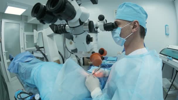 Cirujano mirando al microscopio en el ojo de la paciente femenina en el quirófano. Médico que usa microscopio durante el proceso de cirugía ocular, tratamiento de cataratas y corrección de dioptrías. - Metraje, vídeo
