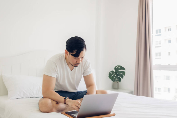 Man is sitting on the bed and working on his laptop. - Fotografie, Obrázek