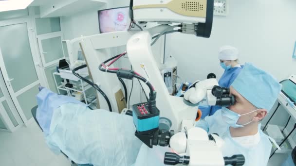 Χειρουργός που εξετάζει το μικροσκόπιο στο μάτι μιας γυναίκας ασθενούς στο χειρουργείο. Γιατρός που χρησιμοποιεί μικροσκόπιο κατά τη διάρκεια χειρουργικής επέμβασης στα μάτια, θεραπεία καταρράκτη και διόρθωση διόπτερου. - Πλάνα, βίντεο