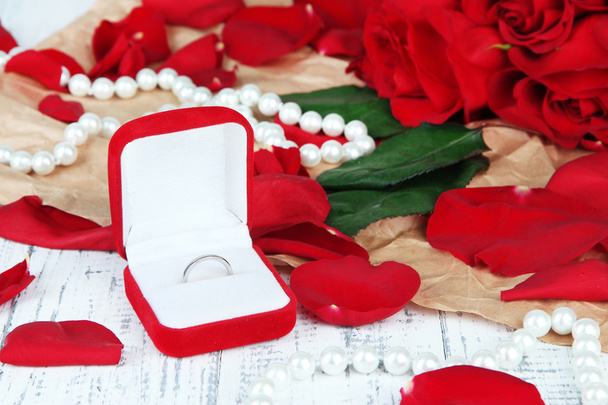 Ring surrounded by roses and petals on wooden table close-up - Foto, Bild