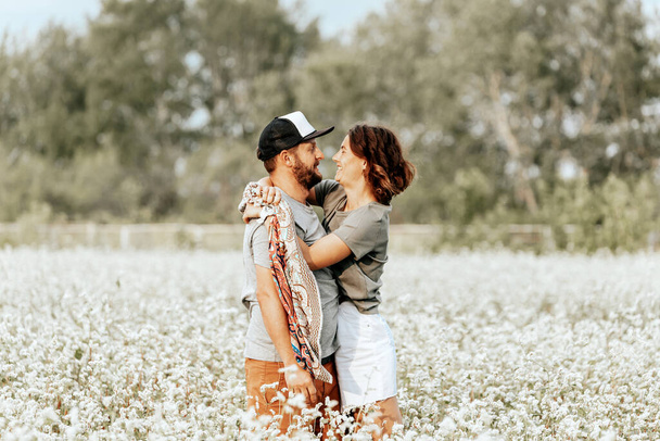 Outdoor atmospheric family portrait of a young beautiful couple on a white field with flowers.   Livestyle walking concept. Creative portrait of a family in nat - Photo, Image