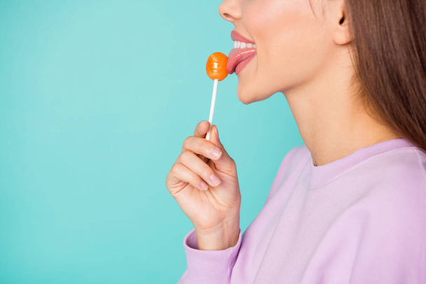 Cropped profile photo of funny lady hold lollipop hand sweets addicted person lick tasty candy tongue wear violet sweater isolated vibrant teal color background - Фото, зображення