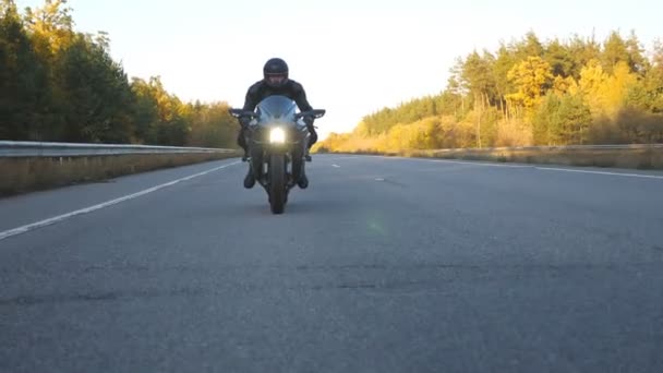 オートバイ愛好家は田舎道でバイクレースをしている。高速道路で現代のスポーツバイクに乗ってヘルメットで若い男。旅行中にバイクを運転する男。冒険の概念。フロントビューを閉じる - 映像、動画