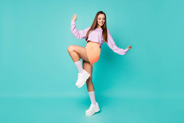 Full body profile photo of funky cool lady raise leg good mood enjoy party dancing youth moves wear purple cropped sweater orange skirt shoes long socks isolated teal color background - 写真・画像