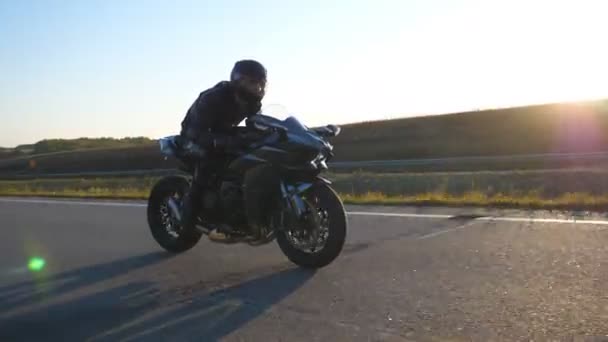 太陽が背景にフレアと高速道路で現代のスポーツバイクに乗って男。オートバイ愛好家は田舎道でバイクレースをしている。旅行中にバイクを運転する男。自由の概念. - 映像、動画
