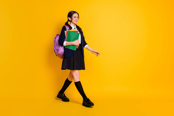 Full length photo of positive a-level student girl hold many copybooks bag rucksack go walk lecture wear blazer skirt isolated over bright shine color background - Foto, immagini