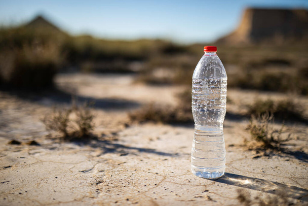 Unetikettierte Plastikwasserflasche auf trockenem Boden in menschenleere Landschaft mit Kopierraum - Foto, Bild