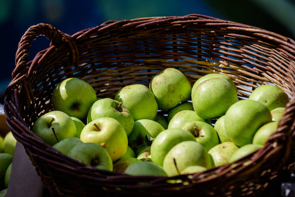 Ομάδα από φρέσκα πράσινα μήλα σε ένα ξύλινο καλάθι, διαθέσιμο προς πώληση σε μια αγορά τροφίμων δρόμο, φυσικό υπόβαθρο, απαλή εστίαση - Φωτογραφία, εικόνα