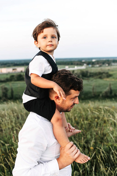 Dad carries toddler on his shoulders outdoors - Foto, immagini