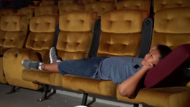 Een jongen liggend op fauteuil in de bioscoop. - Video