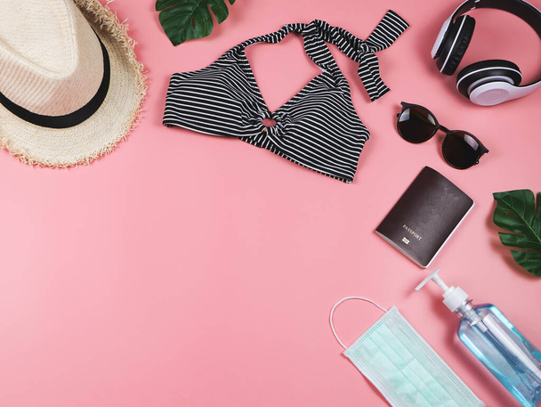 COVID-19 prevención, verano y nuevo concepto normal, vista superior del traje de baño bikini y accesorios de vacaciones de las mujeres con máscara quirúrgica y gel desinfectante sobre fondo rosa
. - Foto, Imagen