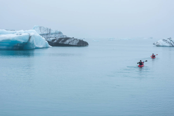 JOKULSARLON, ICELAND - MAY 22, 2019: Man paddling in a kayak in the freezing waters of Jokulsarlon glacier lagoon between icebergs - Zdjęcie, obraz