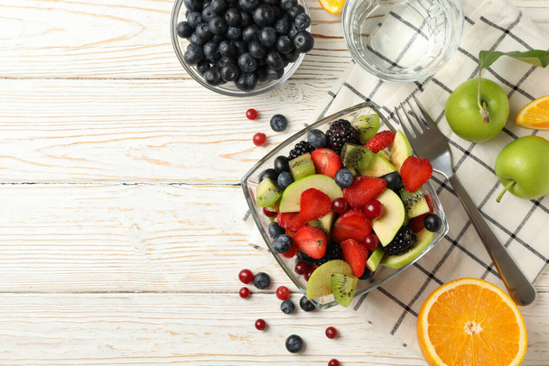 Composición con taza de ensalada de frutas frescas sobre mesa de madera blanca, vista superior
 - Foto, Imagen