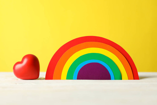 Hart en LGBT regenboog op witte tafel tegen gele achtergrond - Foto, afbeelding