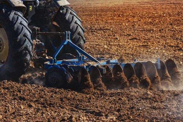 Landwirtschaft, Traktor zur Vorbereitung von Land mit Saatbeet-Kultivierer als Teil der Vorsaat-Aktivitäten in der Frühjahrssaison der landwirtschaftlichen Arbeiten auf landwirtschaftlichen Flächen. - Foto, Bild